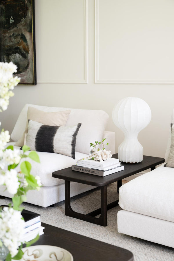 Modernt vardagsrum med vit soffa, svart soffbord, vit skulpturlampa och dekorativa kuddar i neutrala färger