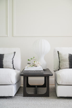 Minimalistisk vardagsrumsinteriör med två vita fåtöljer, svart sidobord och dekorativa böcker med lampa