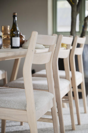 Ljusa trästolar med stoppad sits i beige tyg vid matbord med vinflaskor och glas