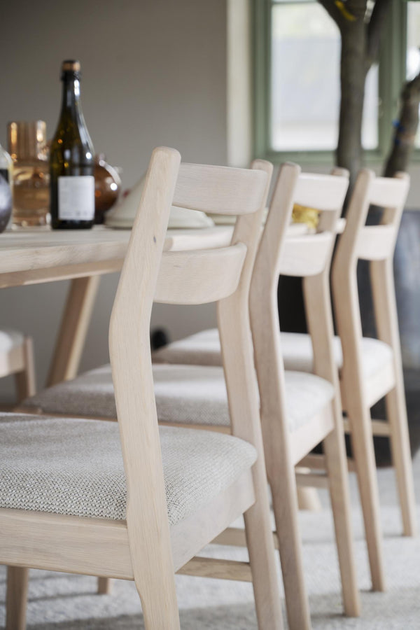 Ljusa trästolar med stoppad sits i beige tyg vid matbord med vinflaskor och glas