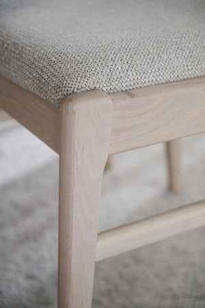 Närbild på pall med grå tygklädsel och ljust trä, detalj av ben och sits i skandinavisk design