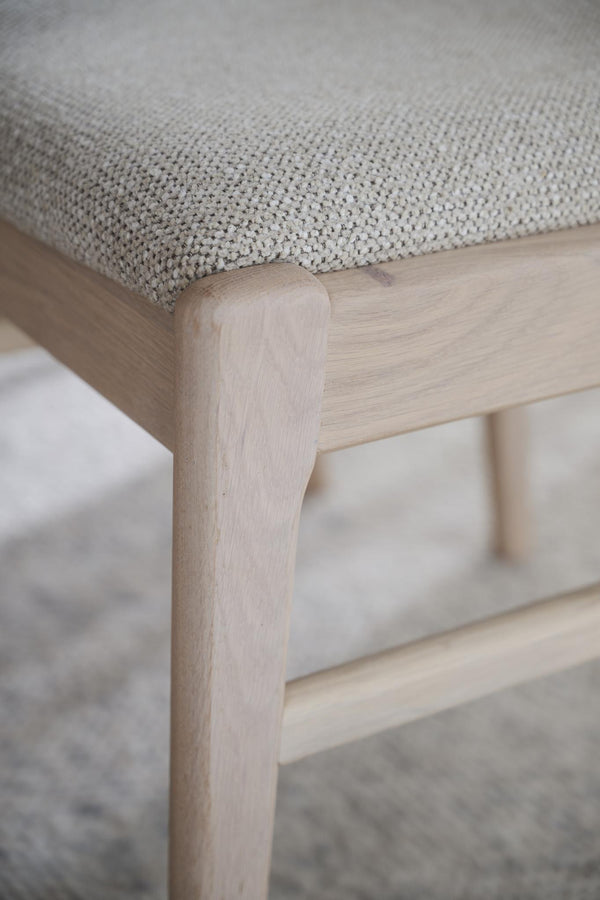 Närbild på pall med grå tygklädsel och ljust trä, detalj av ben och sits i skandinavisk design