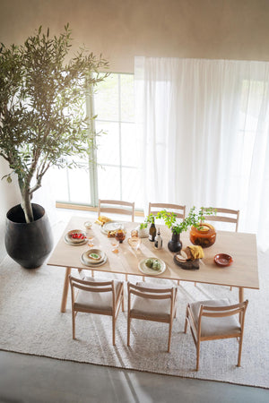 Matbord i ljust trä med stolar i skandinavisk stil, dukat med tallrikar och växter i minimalistisk matsal