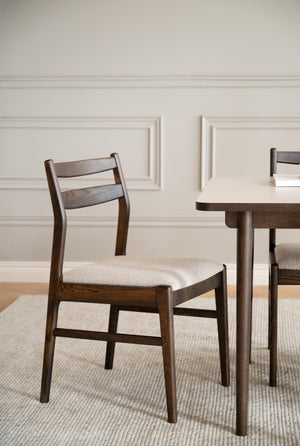 Matstol i mörkbejsat trä med stoppad sits i ljust tyg, vid matbord mot vit panel