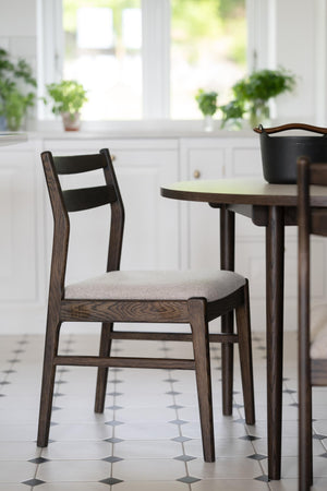 Mörkbrun matstol med stoppad sits i ljusgrått tyg vid runt matbord i modern skandinavisk stil