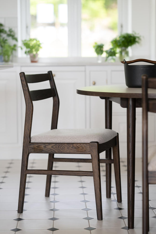 Mörkbrun matstol med stoppad sits i ljusgrått tyg vid runt matbord i modern skandinavisk stil