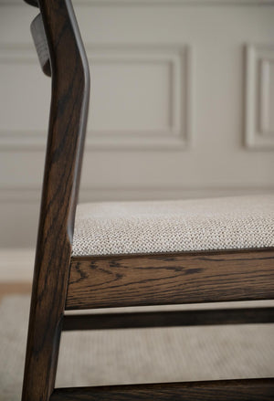 Närbild på stolsben i mörkt trä med grå stoppad sits och vit skåpsinredning i bakgrunden