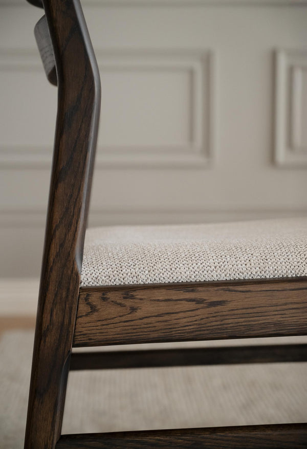 Närbild på stolsben i mörkt trä med grå stoppad sits och vit skåpsinredning i bakgrunden