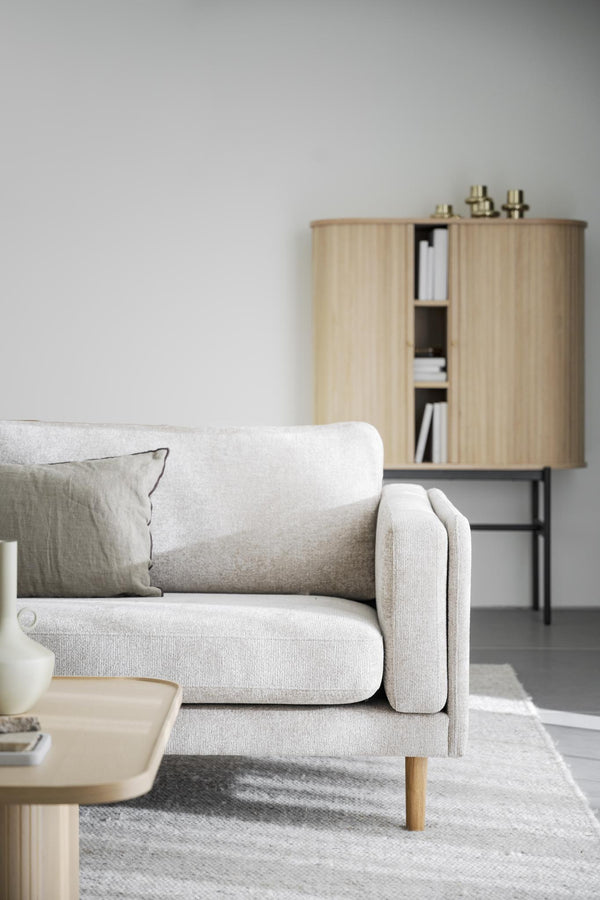 Ljusgrå tvåsitssoffa med träben och dekorativ kudde i skandinavisk vardagsrumsmiljö med träskåp