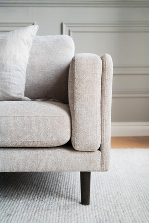 Beige sammetssoffa med kuddor och smala armstöd i modernt vardagsrum