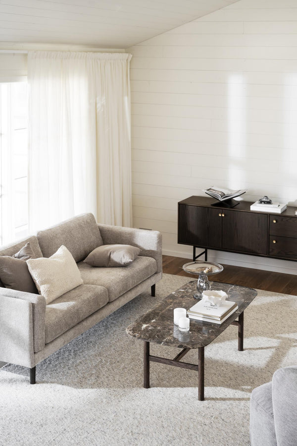 Ljust vardagsrum med grå soffa, marmorbord, mörk skänk och vita väggar i shiplap-stil