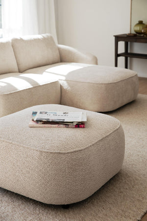 Beige boucle puff och sittpuff med tidningar i ljust vardagsrum med fåtölj och sidebord