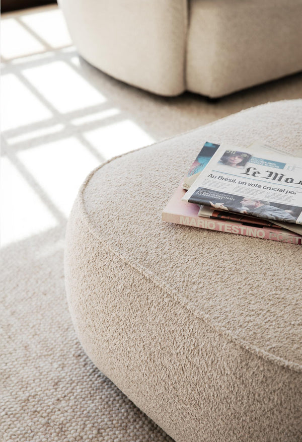 Rund sittbänk i beige bouclé med tidningar på ljust mattor i modernt vardagsrum