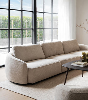 Beige boucle soffa med organiska former i modernt vardagsrum med stora industrifönster och minimalistisk inredning