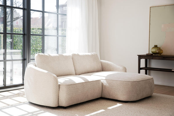 Beige bouclésoffa med schäslong i ljust vardagsrum med stora fönster och minimalistisk inredning