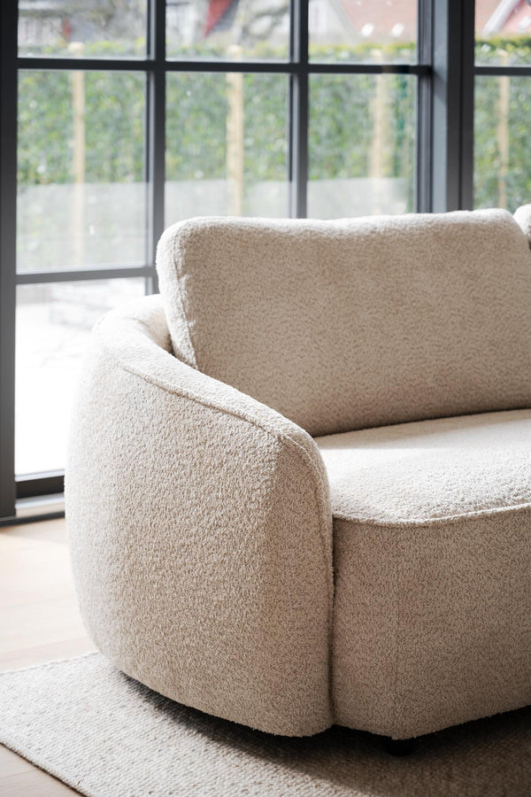 Beige fåtölj i teddy-tyg med rundade former framför stora fönster med svarta spröjs