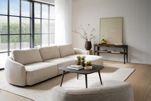 Beige bouclésofa med rundad form i minimalistiskt vardagsrum med stora fönster och mörkt soffbord