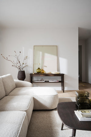 Minimalistiskt vardagsrum med beige soffa, guldspegel och konsoltbord i mörkt trä