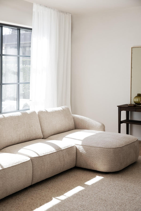 Beige boucle soffa med puff i minimalistiskt vardagsrum med vita väggar och ljusinsläpp från fönster