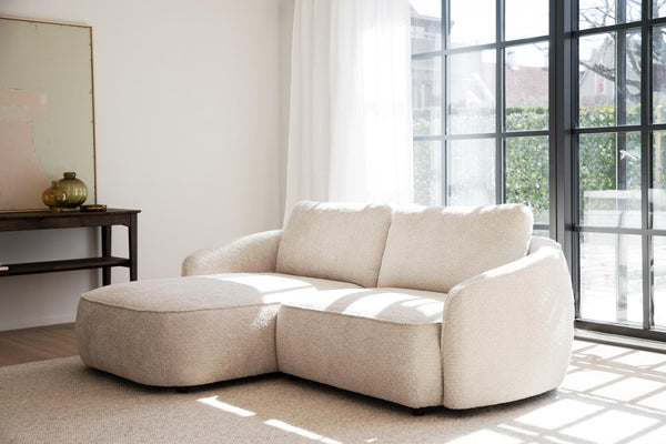 Beige boucle-soffa med schäslong i ljust vardagsrum med stora fönster och minimalistisk inredning