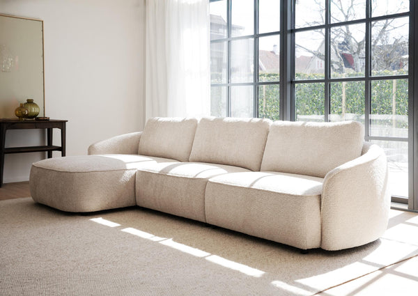 Beige modulsoffa med schäslong i ljust vardagsrum med stora fönster och naturligt ljus