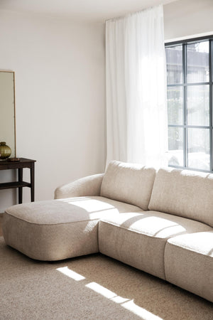 Beige bouclé modulsoffa med schäslong i minimalistiskt vardagsrum med naturligt ljus