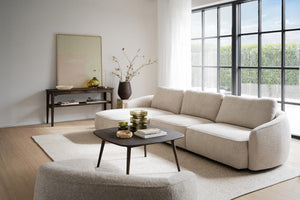 Beige bouclésofa med rundad design och svart soffbord i modernt vardagsrum med stora fönster