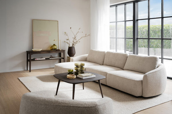 Beige bouclésofa med rundad design och svart soffbord i modernt vardagsrum med stora fönster