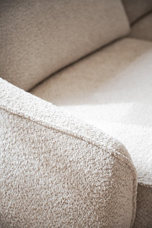 Beige boucléstol med mjuk textur och rundade former, närbild av armstöd och sits