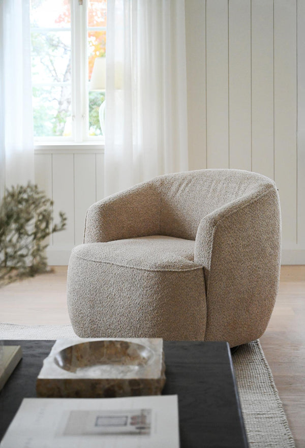 Beige fåtölj i teddyfleece med rundade former vid fönster i ljust vardagsrum