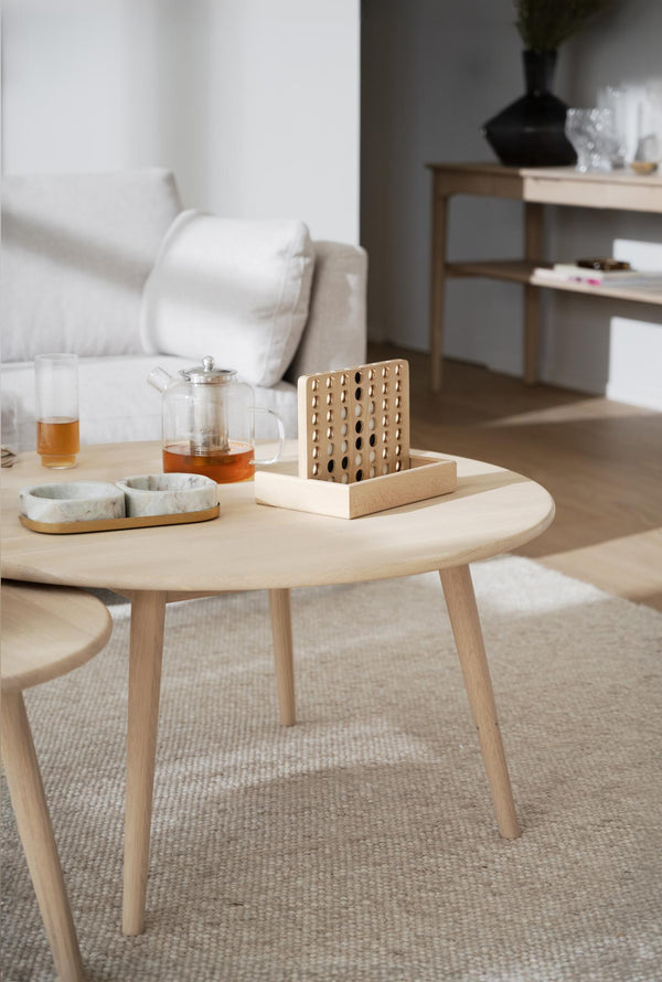 Ljust vardagsrum med runt soffbord i trä, tekanna, glas och dekorativa träobjekt på matta