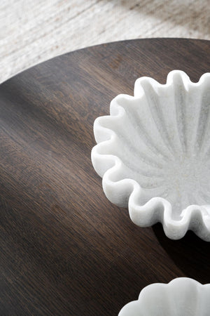 Vit dekorativ marmorskulptur med vågformade kanter på mörkt träbord