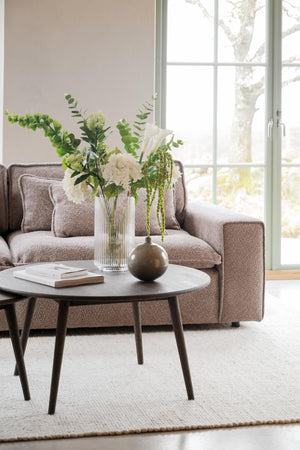 Elegant vardagsrum med brun soffa, runt soffbord i trä och vaser med vita blommor vid fönster