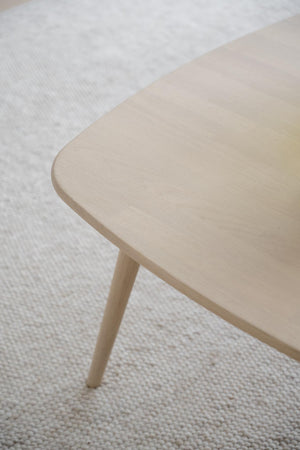 Ljust träbord med rundade hörn och sneda ben på vit textilmatta i skandinavisk stil