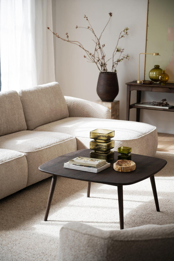 Ljust vardagsrum med beige soffa, svart soffbord i trä, och minimalistisk inredning med gröna glasdetaljer