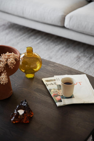 Gul glasvas i rund form på soffbord med kaffekopp och tidning i modern skandinavisk inredning