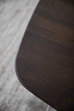 Närbild på rundad bordskant i mörkt trä mot ljust trägolv, detaljerad vy av träets struktur och finish