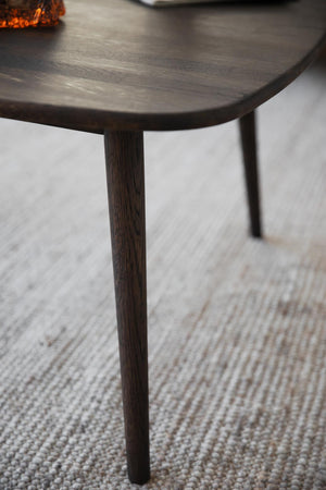 Närbild på mörkbrun träbordskant med konisk bordben på ljus vävd matta