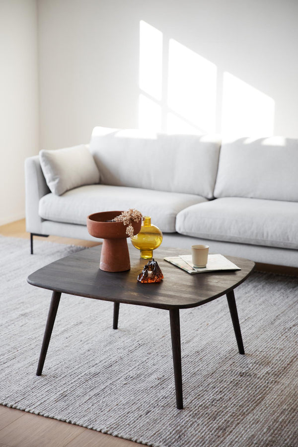 Modernt soffbord i mörkt trä med dekorativa föremål framför grå soffa i minimalistiskt vardagsrum