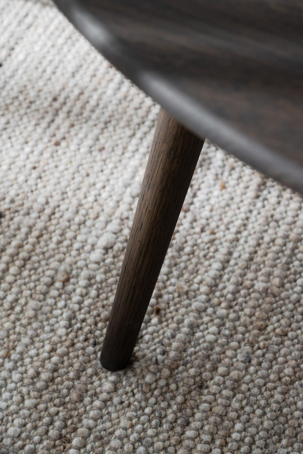 Mörkbrunt träben på möbel mot ljus melerad matta i närbild