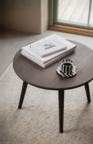 Runt soffbord i mörk ek med böcker och randig kaffekopp på ljus matta vid fönster