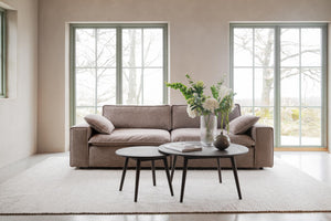 Brun soffa med två runda soffbord framför stora fönster i minimalistiskt vardagsrum