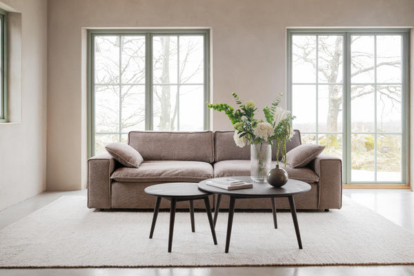 Brun soffa med två runda soffbord framför stora fönster i minimalistiskt vardagsrum