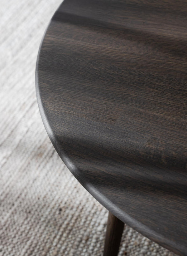Närbild på mörkbrun träbordskiva med synlig åderstruktur och rundad kant, på ljus textilmatta
