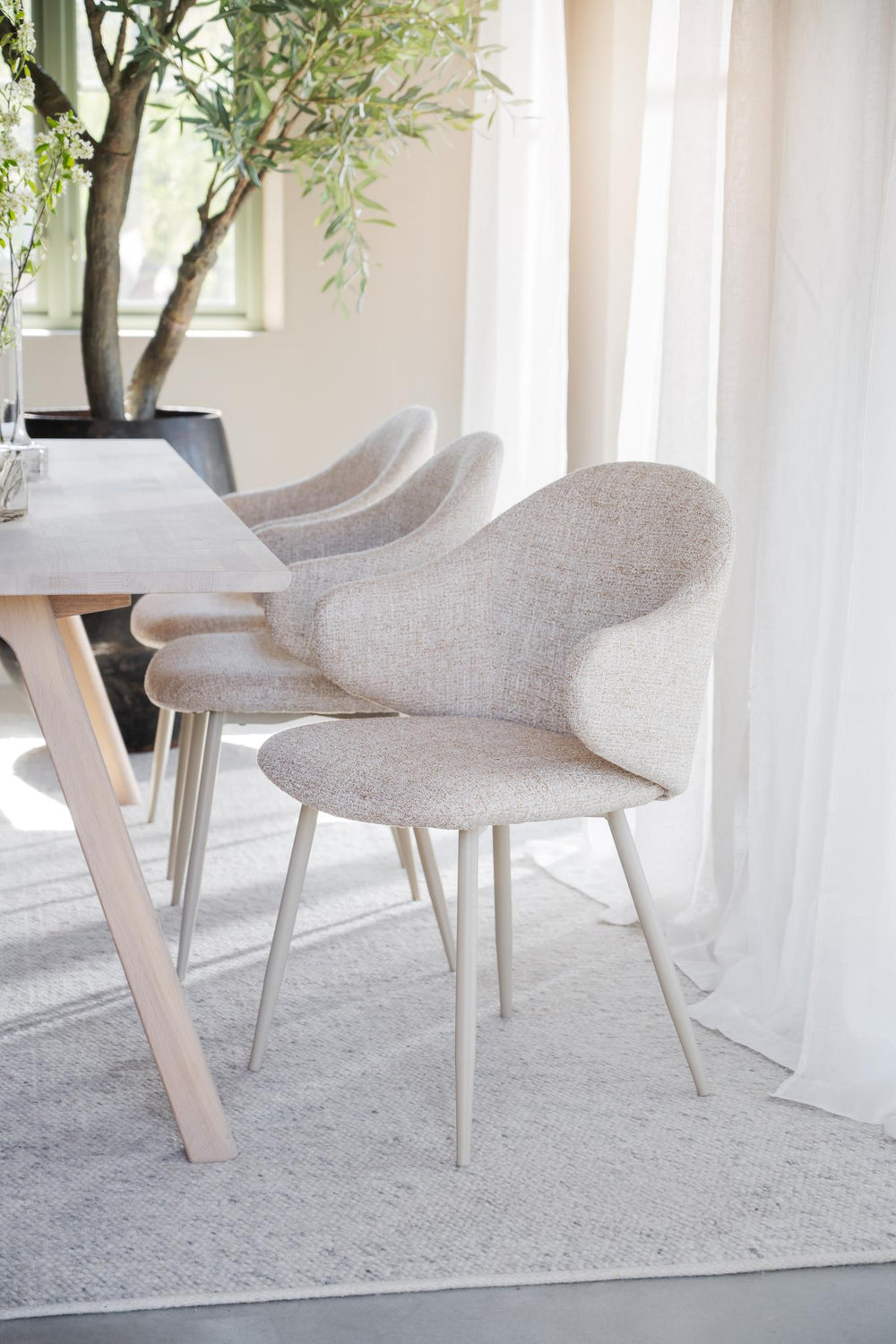 Beige stoppad stol med rundad rygg och smala metallben i ljus färg