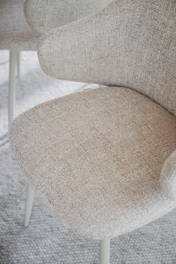 Närbild på beige matstol med stoppad sits och ryggstöd i ljust bouclé-tyg på vit bakgrund