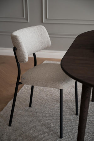Matstol med stoppad sits och rygg i beige bouclé med svarta metallben vid matbord
