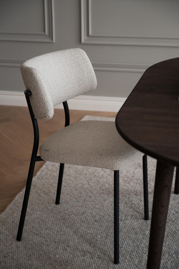 Matstol med stoppad sits och rygg i beige bouclé med svarta metallben vid matbord