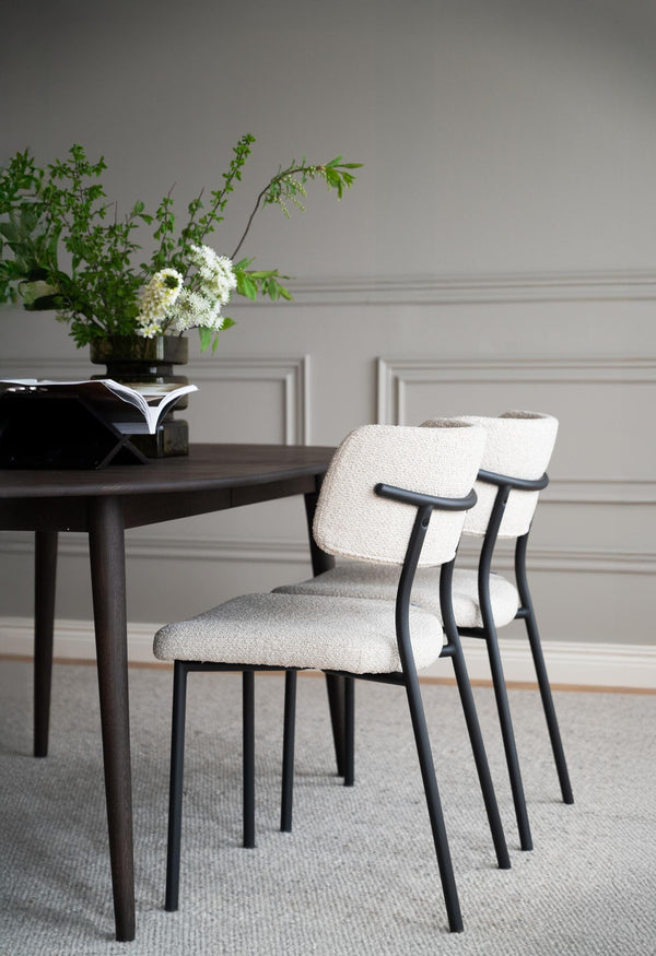 Matbord i mörkt trä med två stolar i bouclé och svarta ben i elegant matsal med ljus väggpanel