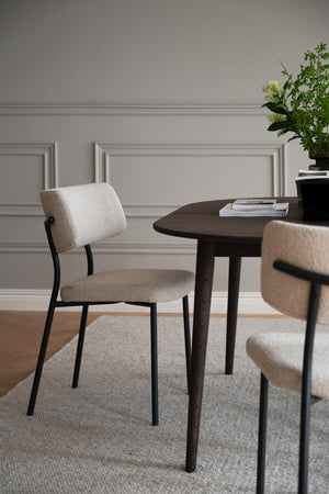 Beige stol med svarta ben vid mörkt matbord i modern matsal med ljusgrå vägg